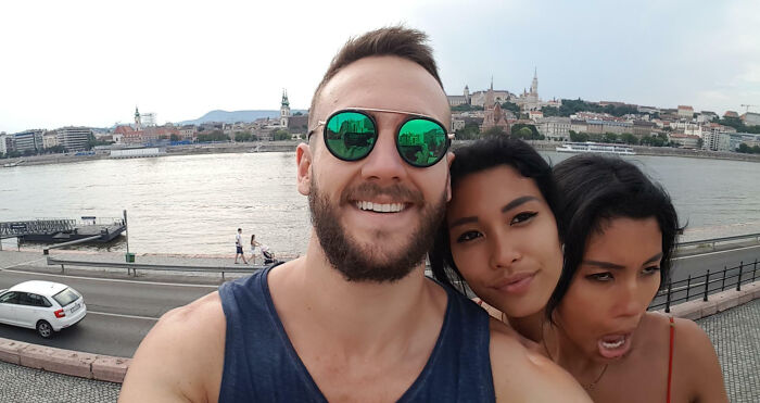 Three friends taking a selfie near a river with cityscape in the background, showcasing interesting pics that answer questions.