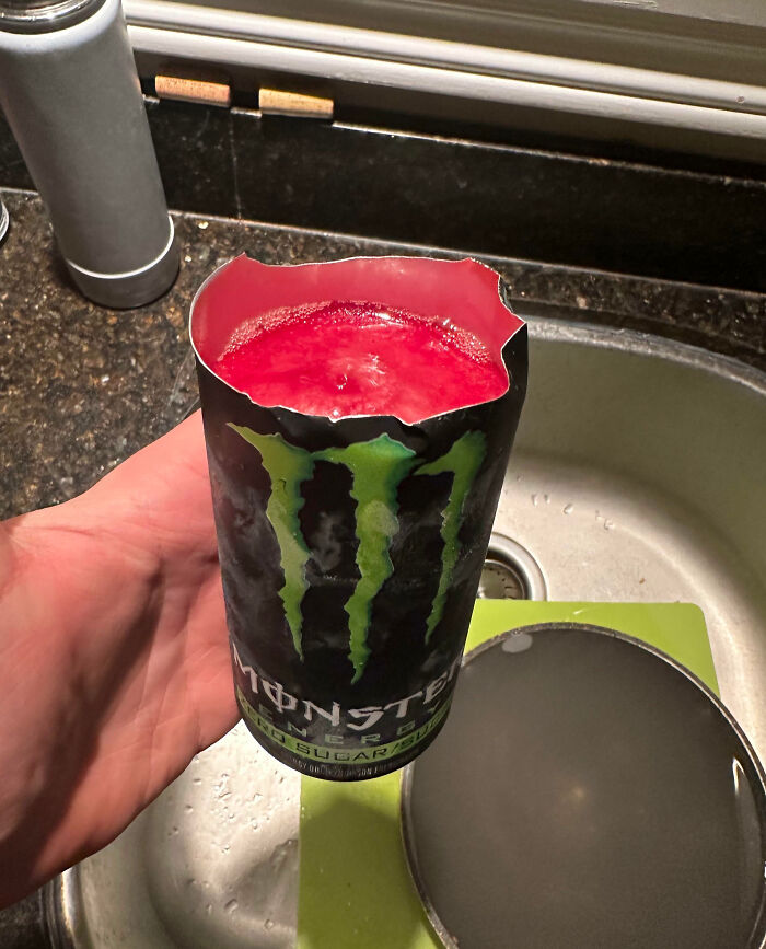 Hand holding a Monster energy drink can cut open at the top revealing the red liquid inside, interesting pics answer questions.