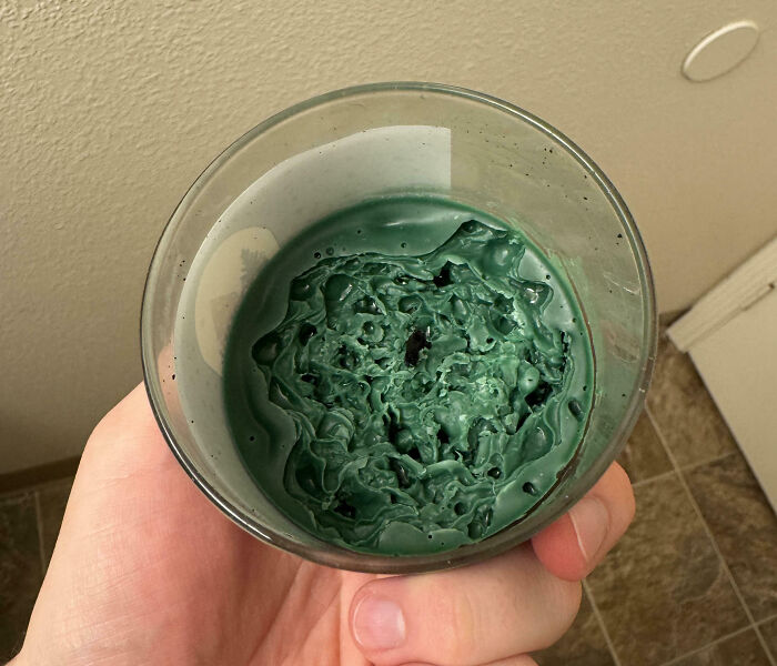 Hand holding a glass with melted green wax, showcasing an interesting pic that answers questions you didn’t know to ask.