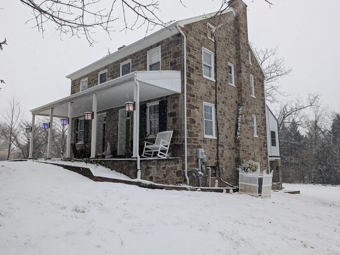 Charming old stone house with covered porch and rocking chair surrounded by snow on a winter day