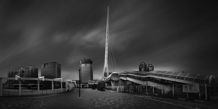 Panoramic view of modern cityscape with tower and unique architectural structures under dramatic sky.