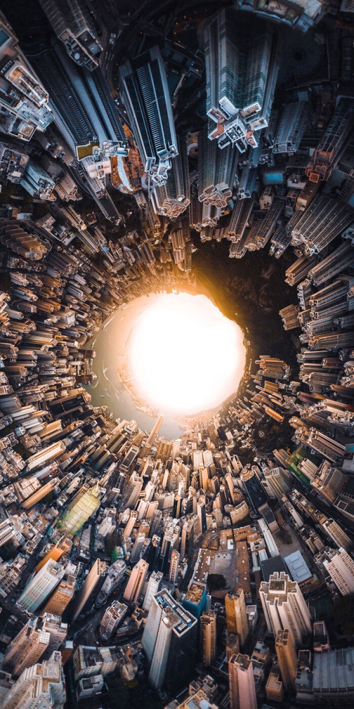 Aerial panoramic masterpiece of a cityscape forming a circular tunnel around a bright glowing center at sunset.