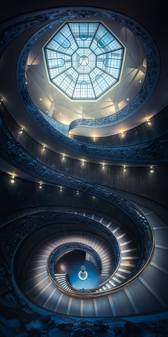 Spiral staircase with ornate railing and illuminated octagonal skylight showcasing panoramic masterpiece architecture.