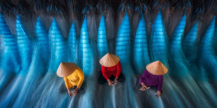 Three people in traditional hats working with blue fishing nets, showcasing panoramic masterpiece photography techniques.