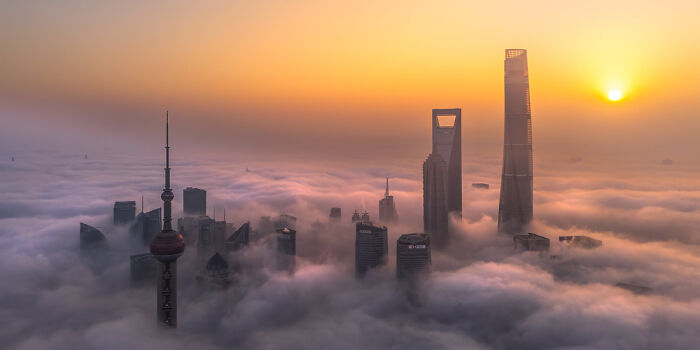 Panoramic cityscape of skyscrapers emerging through dense fog at sunrise, showcasing a stunning Epson Pano Awards masterpiece.