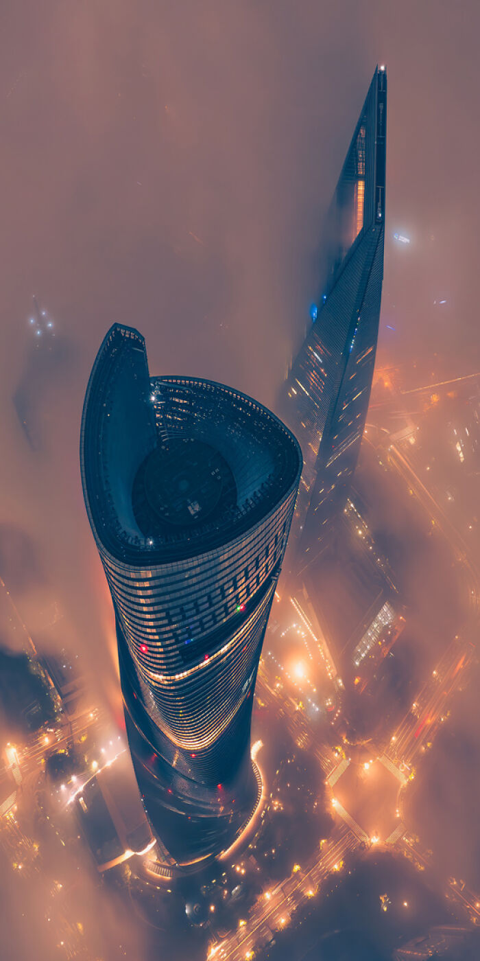 Aerial panoramic view of illuminated skyscrapers piercing through fog in a vibrant cityscape at night.