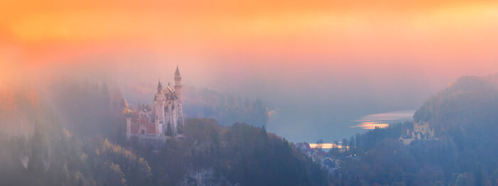 Panoramic masterpiece of a castle on a misty hill at sunrise, showcasing breathtaking colors and serene landscape.