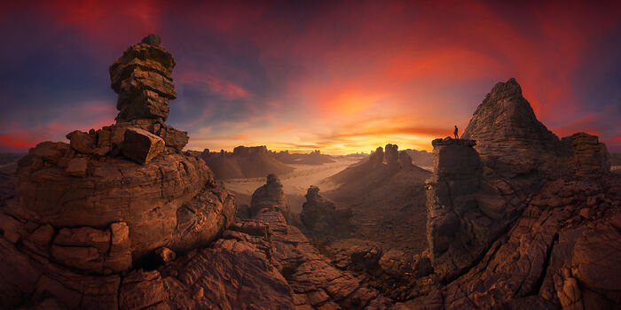 Panoramic masterpiece of a rocky desert landscape at sunset with vibrant orange and purple skies, showcasing natural formations.