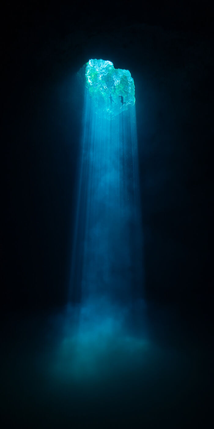 Underwater cave with blue light rays streaming through an opening, showcasing a panoramic masterpiece of nature.