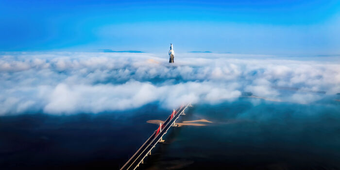 A panoramic view of a bridge and statue emerging through a sea of clouds, showcasing stunning panoramic masterpieces.