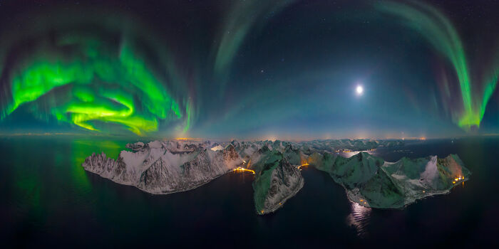 Panoramic masterpiece showing the Northern Lights over a snowy mountainous island at night, winner of Epson Pano Awards 2025.