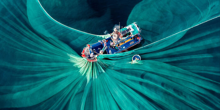 Aerial view of fishing boats spreading large green nets in deep blue waters captured as a panoramic masterpiece.