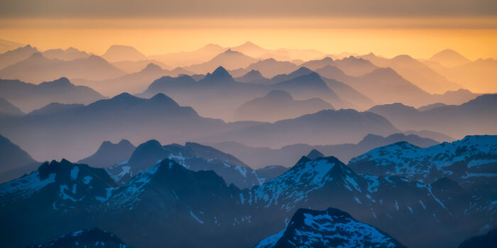 Panoramic mountain landscape at sunset with layers of peaks and soft orange sky, showcasing panoramic masterpieces.