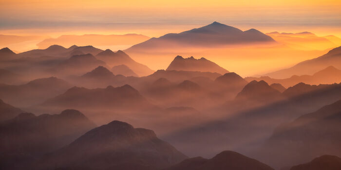 Panoramic masterpiece of layered mountain ranges at sunrise with soft golden light and misty atmosphere in nature landscape.