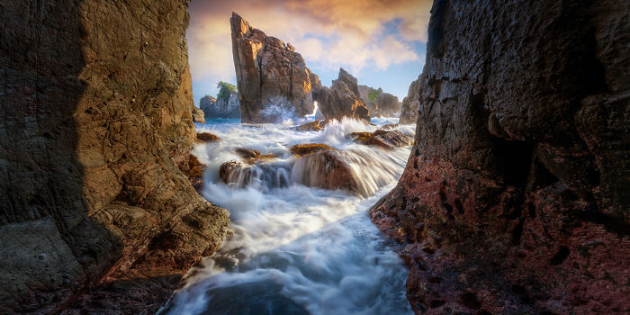 Panoramic masterpiece of rugged coastal rocks with waves crashing through natural arches during golden hour light.