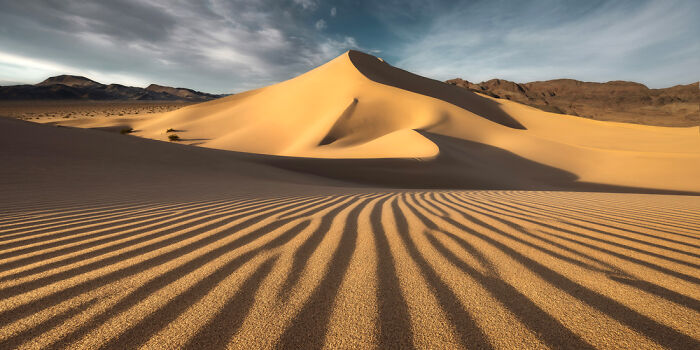 Panoramic masterpiece of a sunlit sand dune with rippled patterns under a blue sky, awarded in Epson Pano Awards 2025.