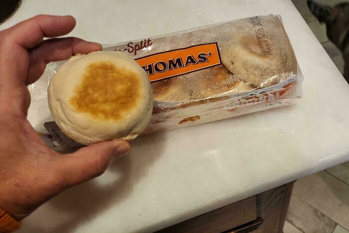 Hand holding an English muffin with packaging showing brand name, illustrating misleading product packaging examples.