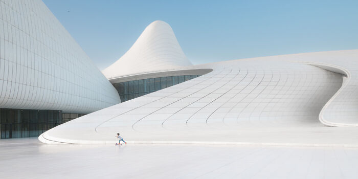 Child riding scooter near sleek futuristic white building under clear blue sky, stunning panoramic masterpiece from Epson Pano Awards