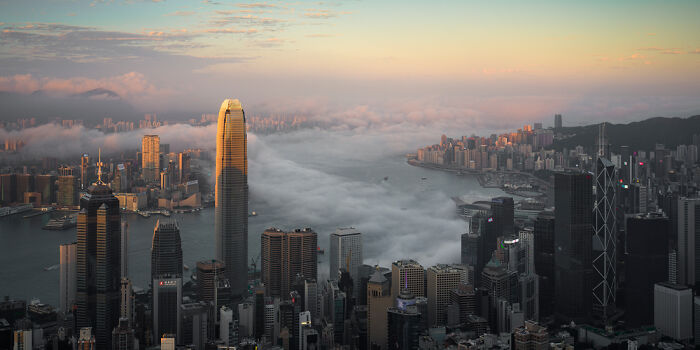 Panoramic cityscape with skyscrapers and a river under a golden sky, showcasing stunning urban views and mist.