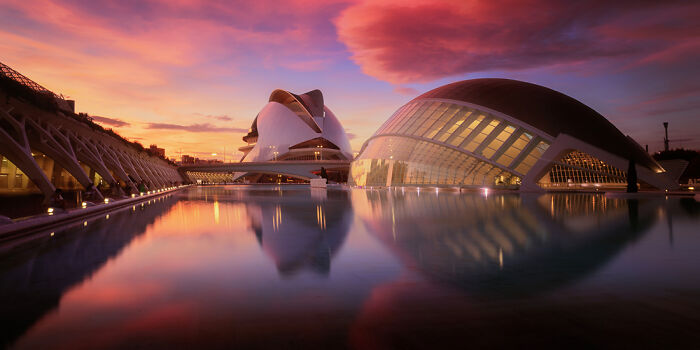 Panoramic masterpiece of modern architecture reflecting in calm water under a vibrant sunset sky at the Epson Pano Awards.