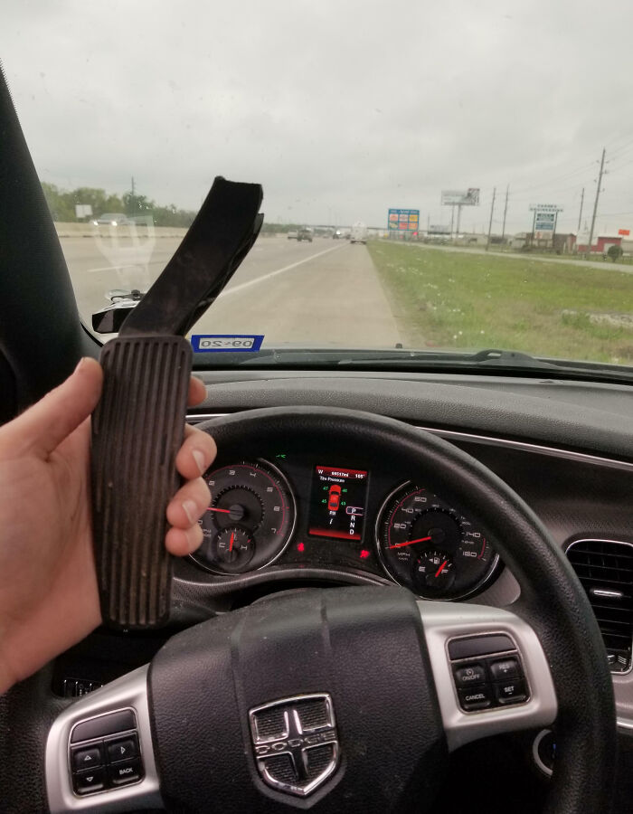Mano sosteniendo pedal roto dentro de un coche Dodge en una carretera con clima nublado, mostrando fotos que pueden empeorar tu día.
