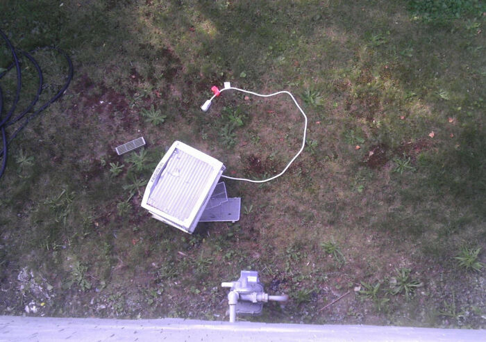 Broken window air conditioner lying on grass next to tangled power cord in a messy outdoor setting.