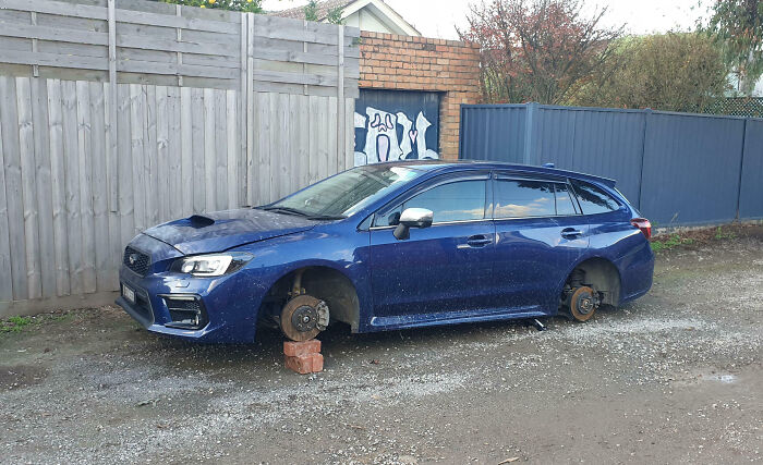 Coche azul sin ruedas apoyado sobre ladrillos en un terreno, muestra que un día horrible puede empeorar radicalmente.