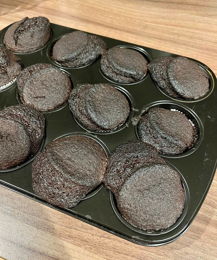 Overbaked chocolate cupcakes overflowed and collapsed in a black muffin tray on a wooden surface messy baking fails