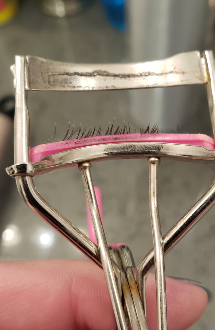 Close-up of an eyelash curler with a few lashes stuck, showing a messy and imperfect beauty tool scene.