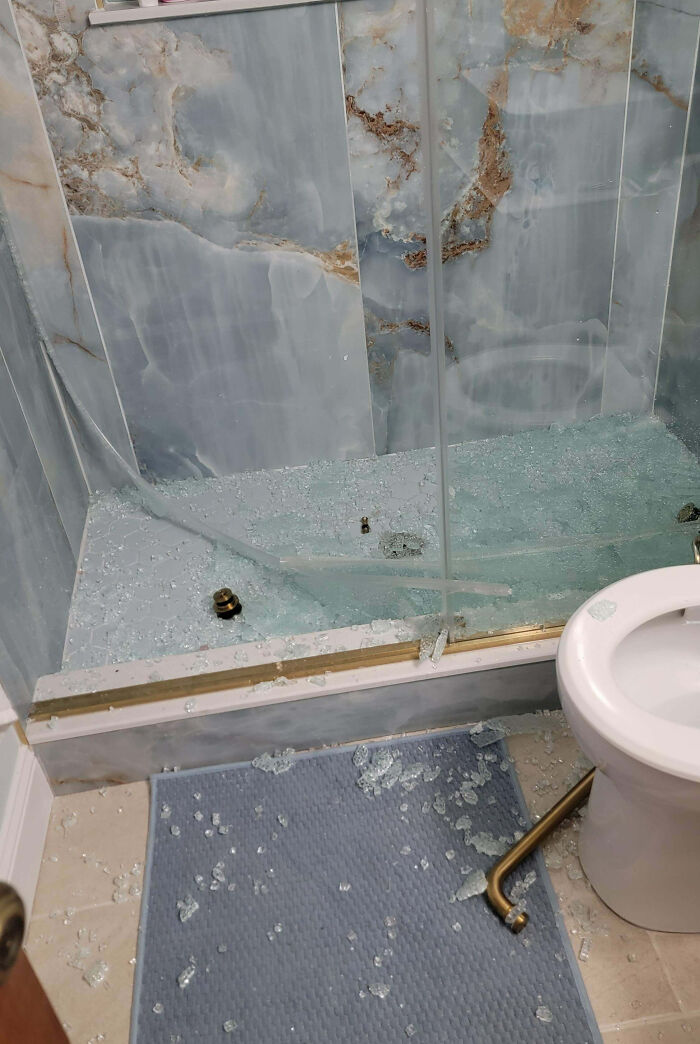 Broken glass shower door shattered on bathroom floor next to toilet, illustrating that today feels like a total mess.