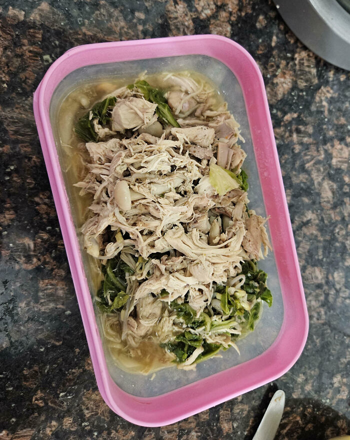 Shredded chicken and greens in a pink container on a kitchen countertop, showing a total mess meal reminder.