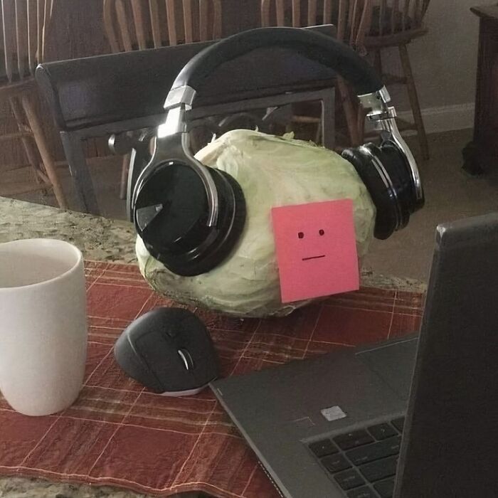 A cabbage with headphones and a sticky note face sitting near a laptop, a quirky image that might need a priest or exorcist.