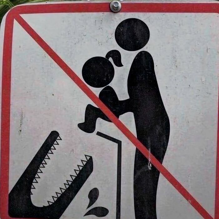 Warning sign showing a person holding a child near a dangerous alligator, an image that might need a priest or an exorcist.