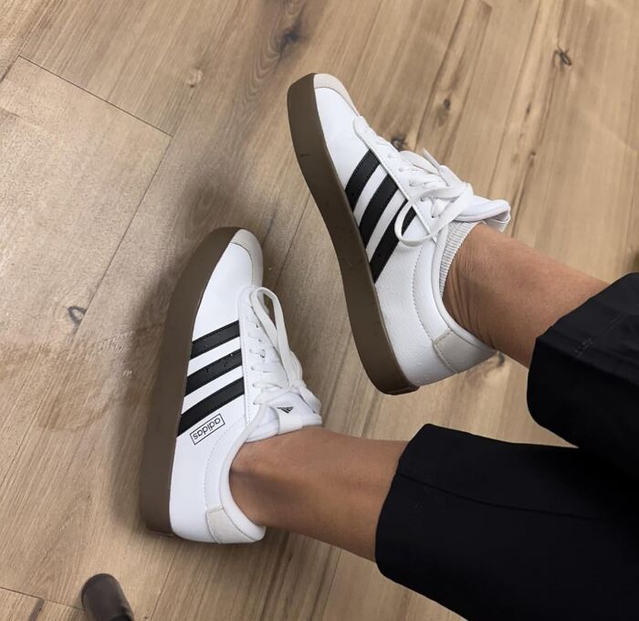 White and black Adidas sneakers worn on feet viewed against a wooden floor, viral products popular during Amazon big deal days.