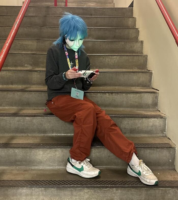 Person with blue hair and a mask sitting on stairs, playing on a mobile device showing viral products popular during Amazon's deal days.