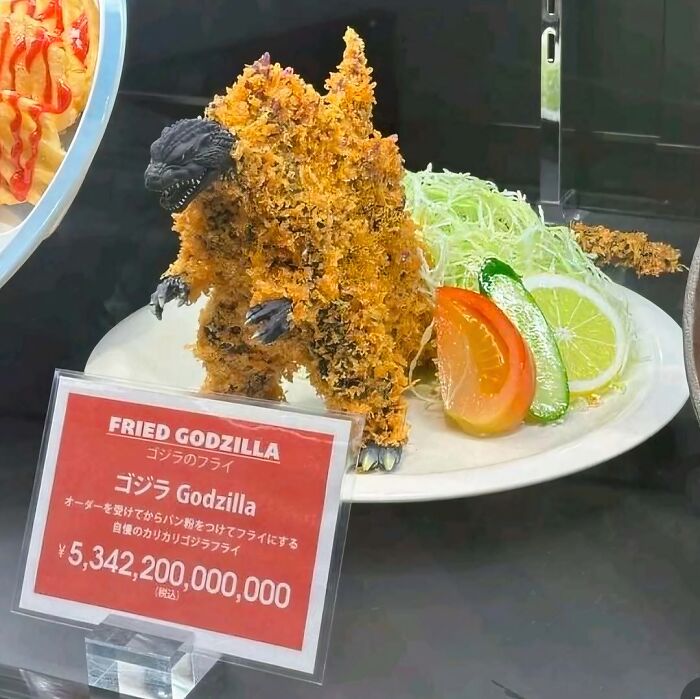 Fried Godzilla shaped dish with crispy coating served with sliced vegetables on a white plate, unusual image needing exorcist.