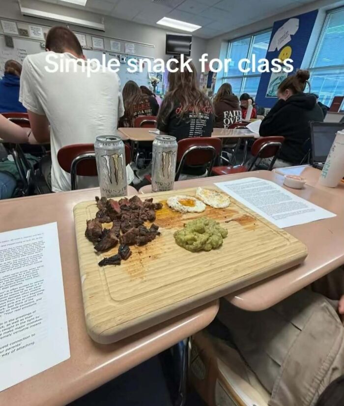 Classroom scene with a shocking snack of cooked meat, eggs, and energy drinks on a cutting board, unusual for school setting.