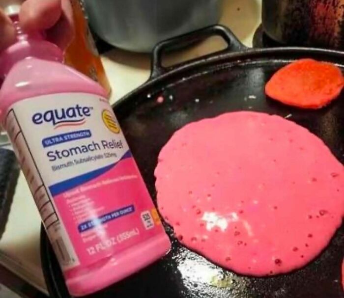 Pink stomach relief medicine bottle next to a bright pink pancake cooking on a black griddle, a strange image that might need a priest.
