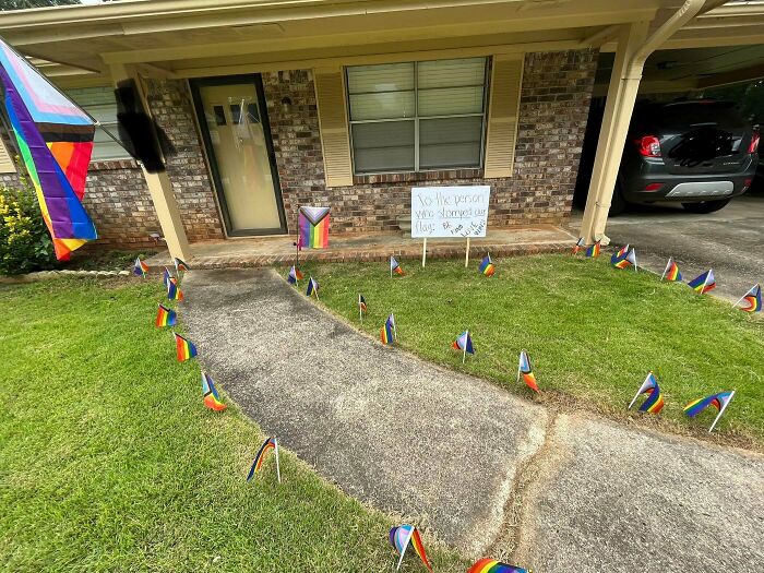 Yard with small pride flags and a sign as an example of petty revenge not worth being a jerk to others.