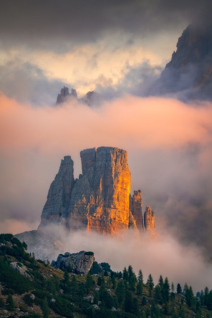 Majestic mountain peaks glowing in sunset light surrounded by mist in a stunning nature photography finals image.