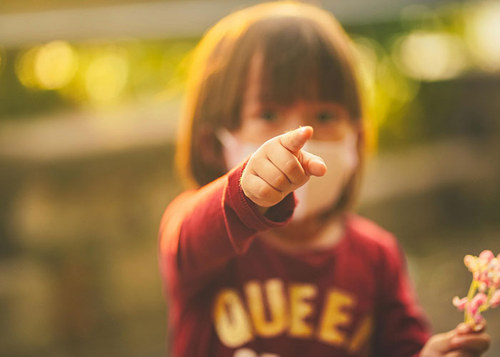 Young child wearing a mask pointing forward outdoors, illustrating moments where kids embarrass their moms badly.