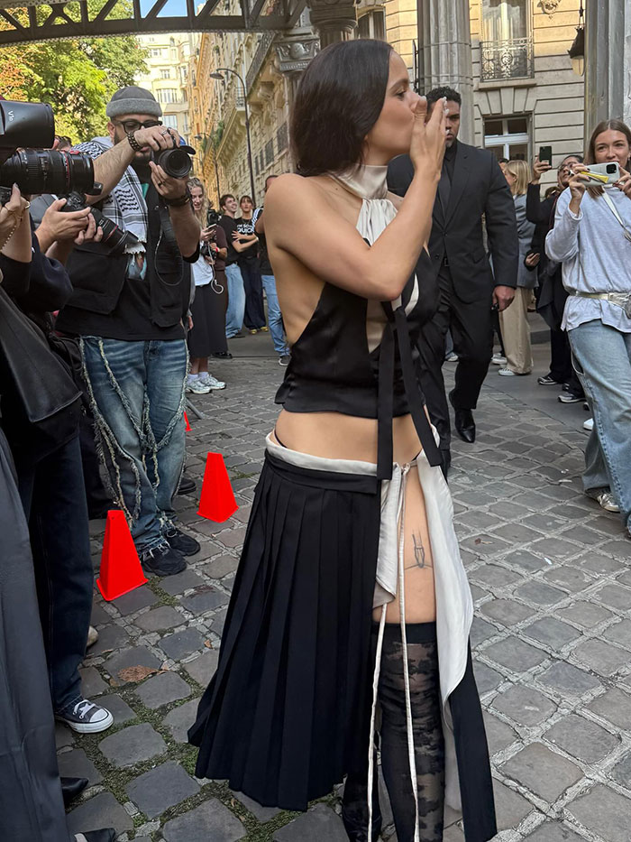 Pop star posing at Paris Fashion Week, surrounded by photographers capturing her bold dyed armpit hair and unique outfit.