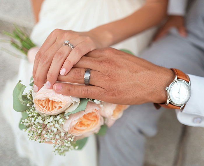 Close-up of married couple's hands with wedding rings holding a bouquet, illustrating benefits of marrying your cousin in UK health guidance.