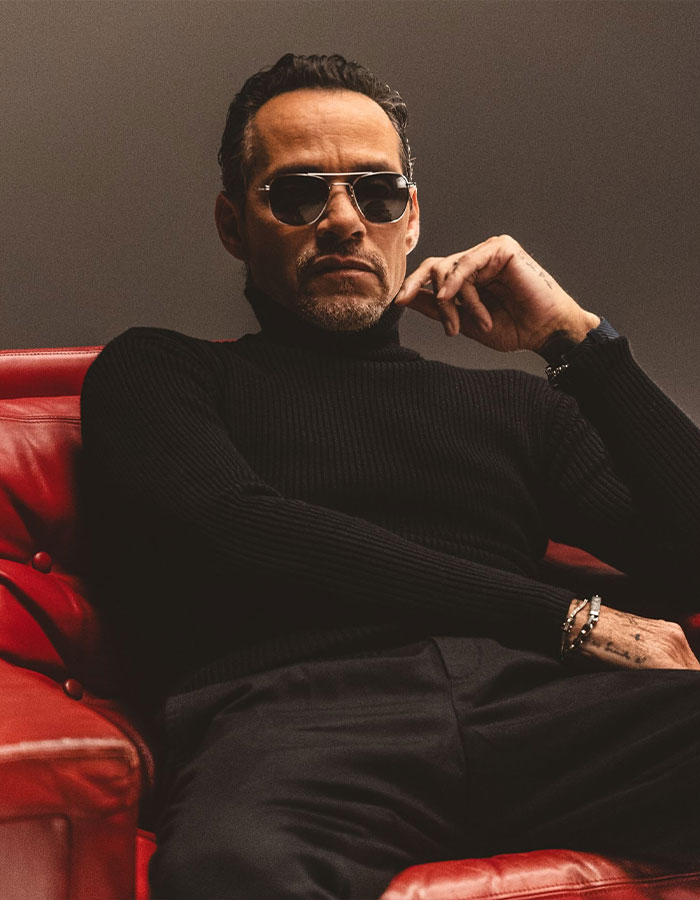 Man wearing sunglasses and black turtleneck sitting on a red chair, representing famous men shorter than fans imagined.