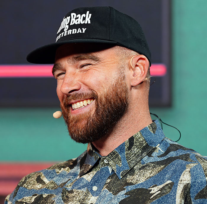 Man smiling and wearing a cap and patterned shirt while speaking, related to Travis Kelce's manhood in new song discussion.