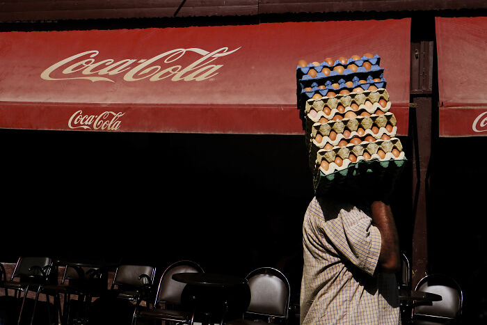 Man carrying stacks of eggs on his head in a vibrant street photography shot capturing life’s unexpected moments.