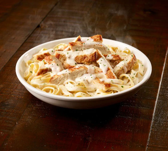 Plate of fettuccine alfredo with grilled chicken on a wooden table, related to American tourist in Italy story.