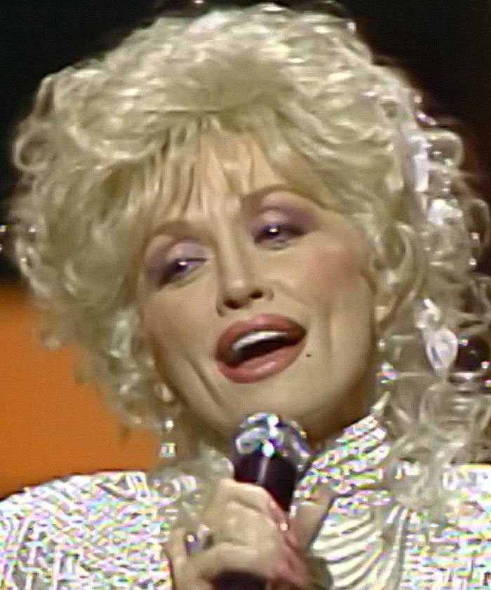 Dolly Parton performing on stage with microphone, highlighting sister raising alarm amid health struggles news.