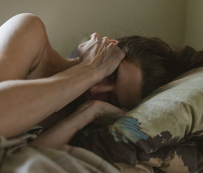 Young girl lying in bed covering her face, symbolizing severe mistreatment at home and escape from abuse situation.