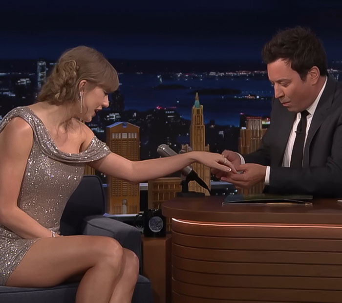 Taylor Swift on a late-night talk show, interacting with the host during an autograph signing segment.